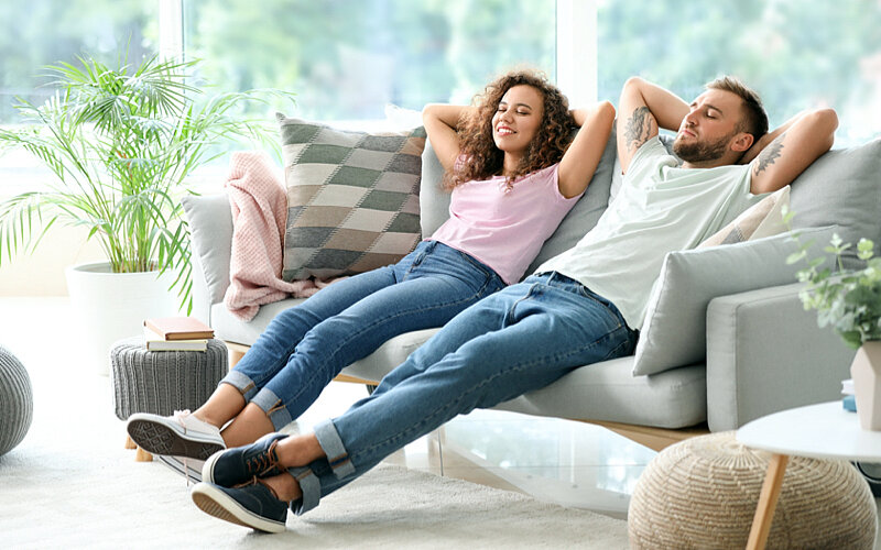 Eine junge Frau und ein junger Mann lehnen sich entspannt auf einem Sofa zurück.