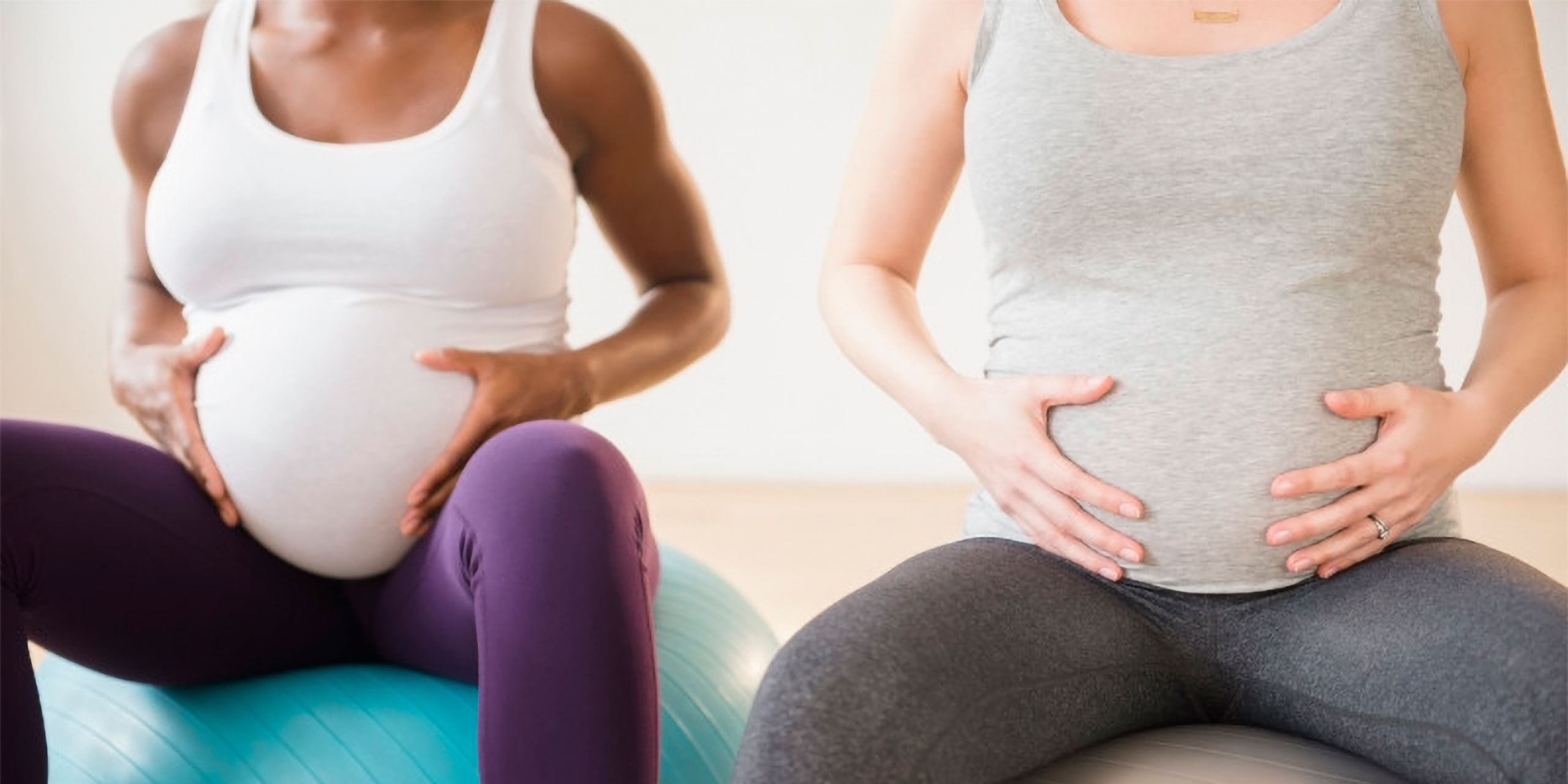 Zwei Schwangere halten sich bei Schwangerschaftsübungen auf Übungsbällen seitlich den Bauch